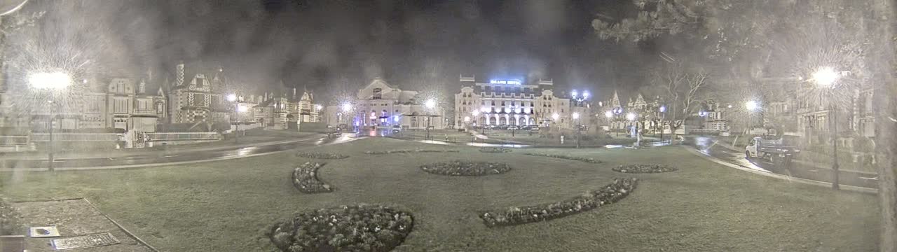 A nighttime view of a town square with several buildings, including a large hotel, lit by streetlights in snowy conditions.