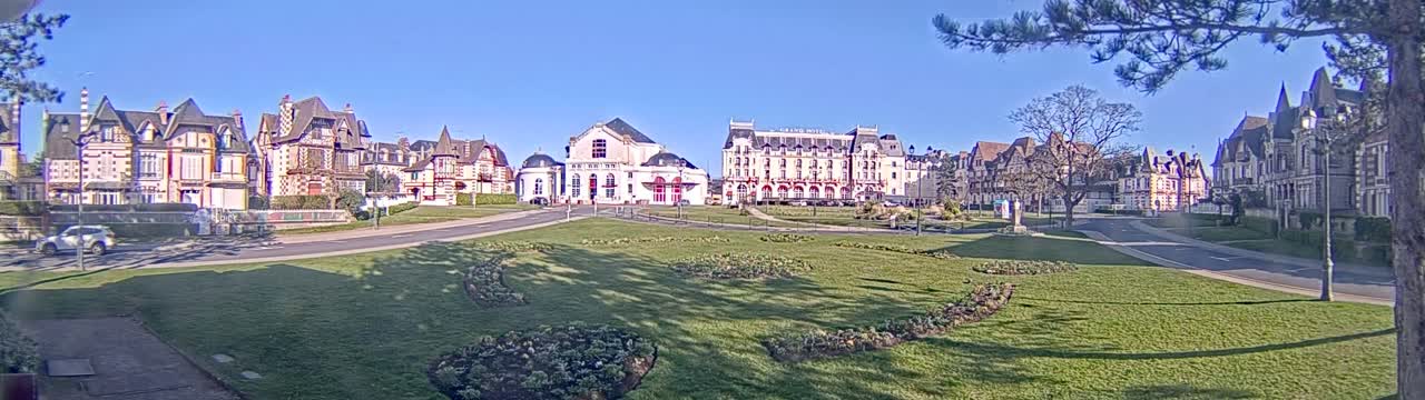 A row of ornate buildings lines a grassy square on a sunny day.