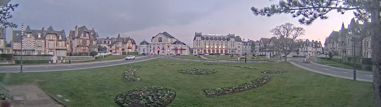A grassy square with flowerbeds is surrounded by several large, ornate buildings under an overcast sky.
