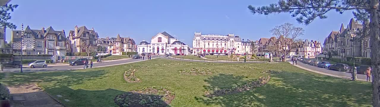 A sunny day reveals a grassy square in front of a row of elegant, multi-story buildings, some with distinctive architectural details.
