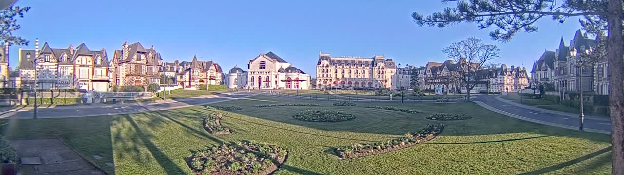 A sunny day reveals a grassy park with manicured flowerbeds in front of several large, ornate buildings.