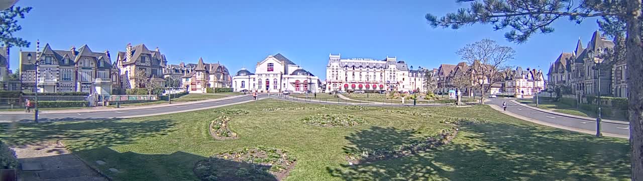 A grassy square with several large buildings and a clear blue sky is visible on a sunny day.