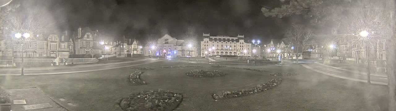 A nighttime view of a town square with several buildings, including a large hotel, illuminated by streetlights in snowy conditions.