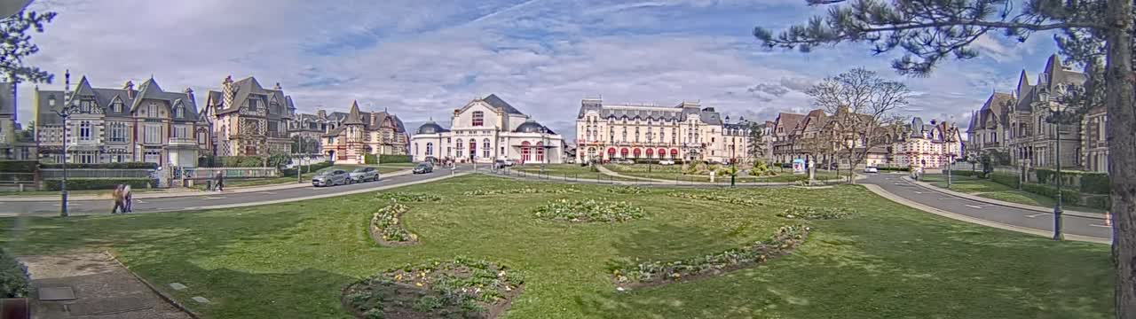 A grassy square is surrounded by several large, ornate buildings under a partly cloudy sky.
