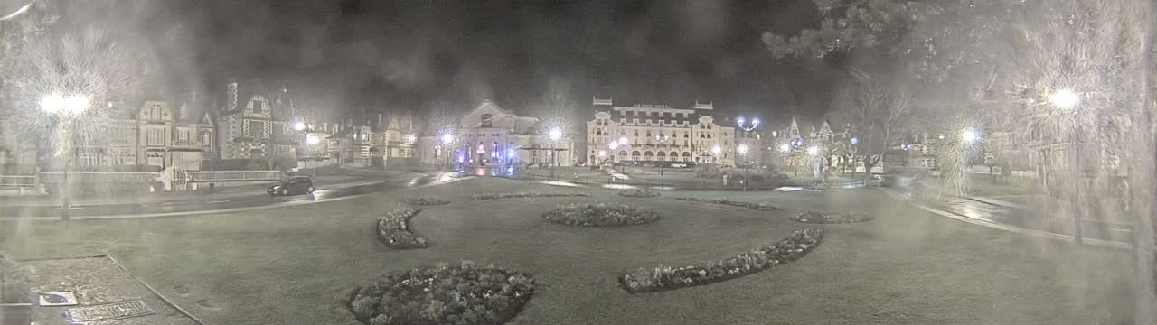 A nighttime scene shows a town square with several buildings, including a large hotel, under snowy conditions.