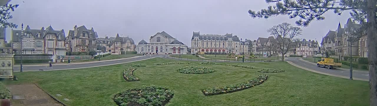 A grassy plaza with flowerbeds is centered in front of several large buildings in a cloudy, overcast setting.