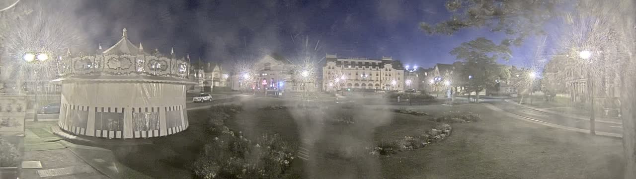 A nighttime view of a carousel and several buildings across a grassy area under a hazy sky.