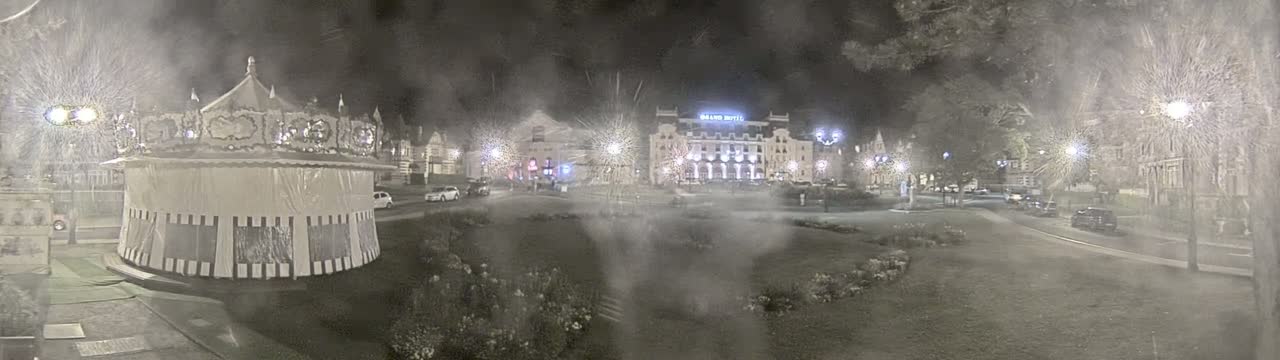 A carousel sits in a hazy, nighttime town square, in front of several buildings, including a large hotel.