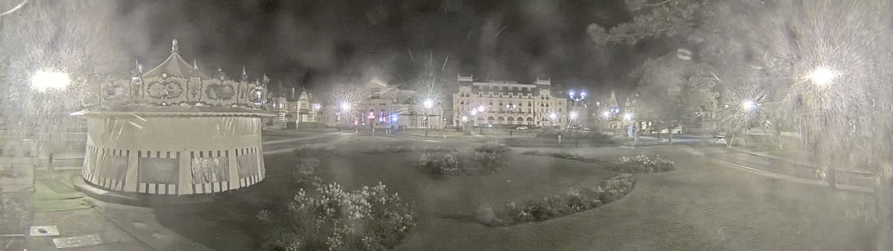 A nighttime scene shows a carousel and several buildings across a grassy area, obscured by heavy snow or rain.