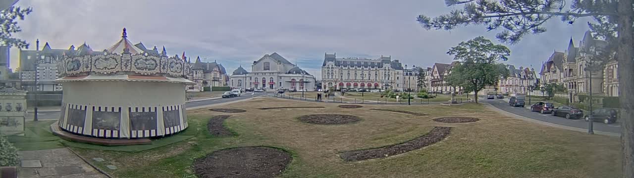 A carousel sits in a town square with several large buildings in the background under an overcast sky.