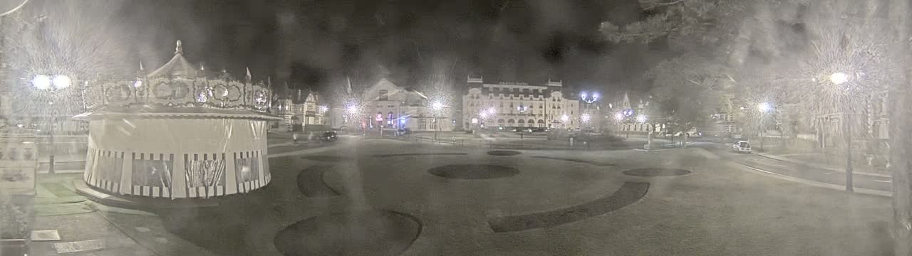 A snow-covered town square at night features a carousel, several buildings, and streetlights.
