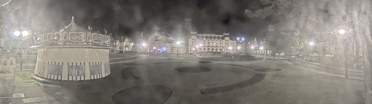 A snow-covered town square at night, featuring a carousel, several buildings, and streetlights.