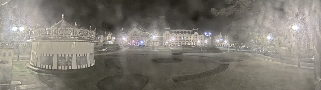 A carousel sits in a snow-covered town square at night, with several buildings and streetlights visible in the background.