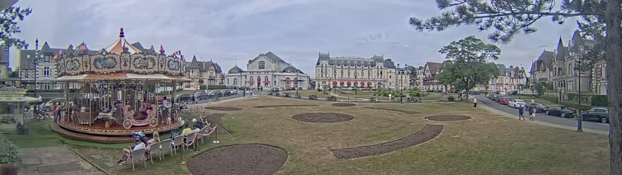 A carousel sits in a town square next to several large buildings on a partly cloudy day.