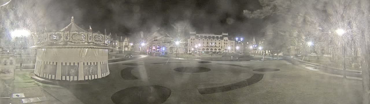 A snow-covered town square at night, featuring a carousel and several buildings, is illuminated by streetlights.