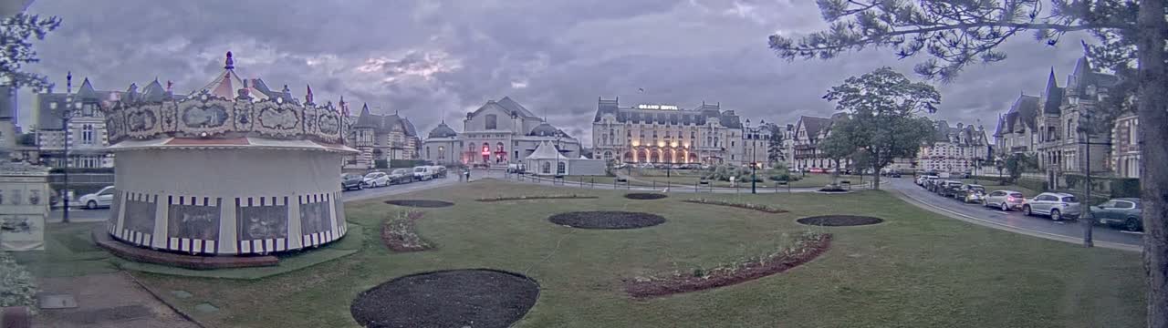 A carousel sits in a town square near several buildings under an overcast sky.