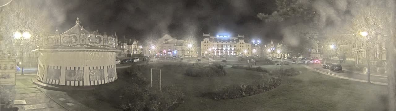 A nighttime scene shows a carousel, several buildings, and a grassy area, all under hazy or foggy conditions.