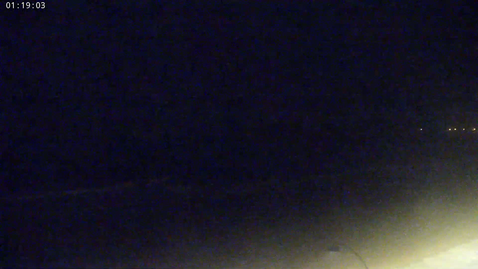 A nighttime, low-light view shows a dark expanse with a few distant lights on the horizon.