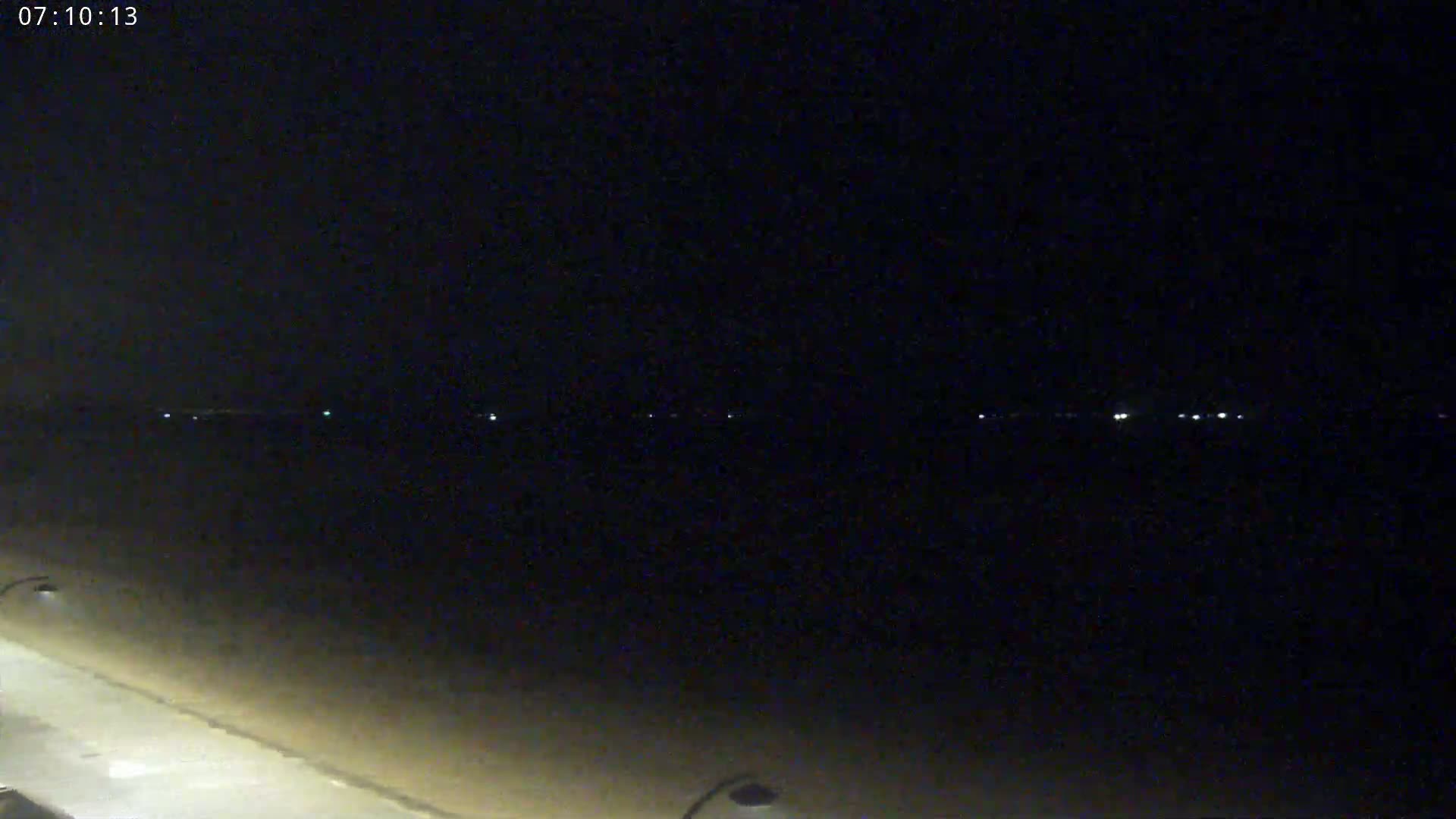 A dark, nighttime beach scene shows a dimly lit shoreline with faint lights visible in the distance.