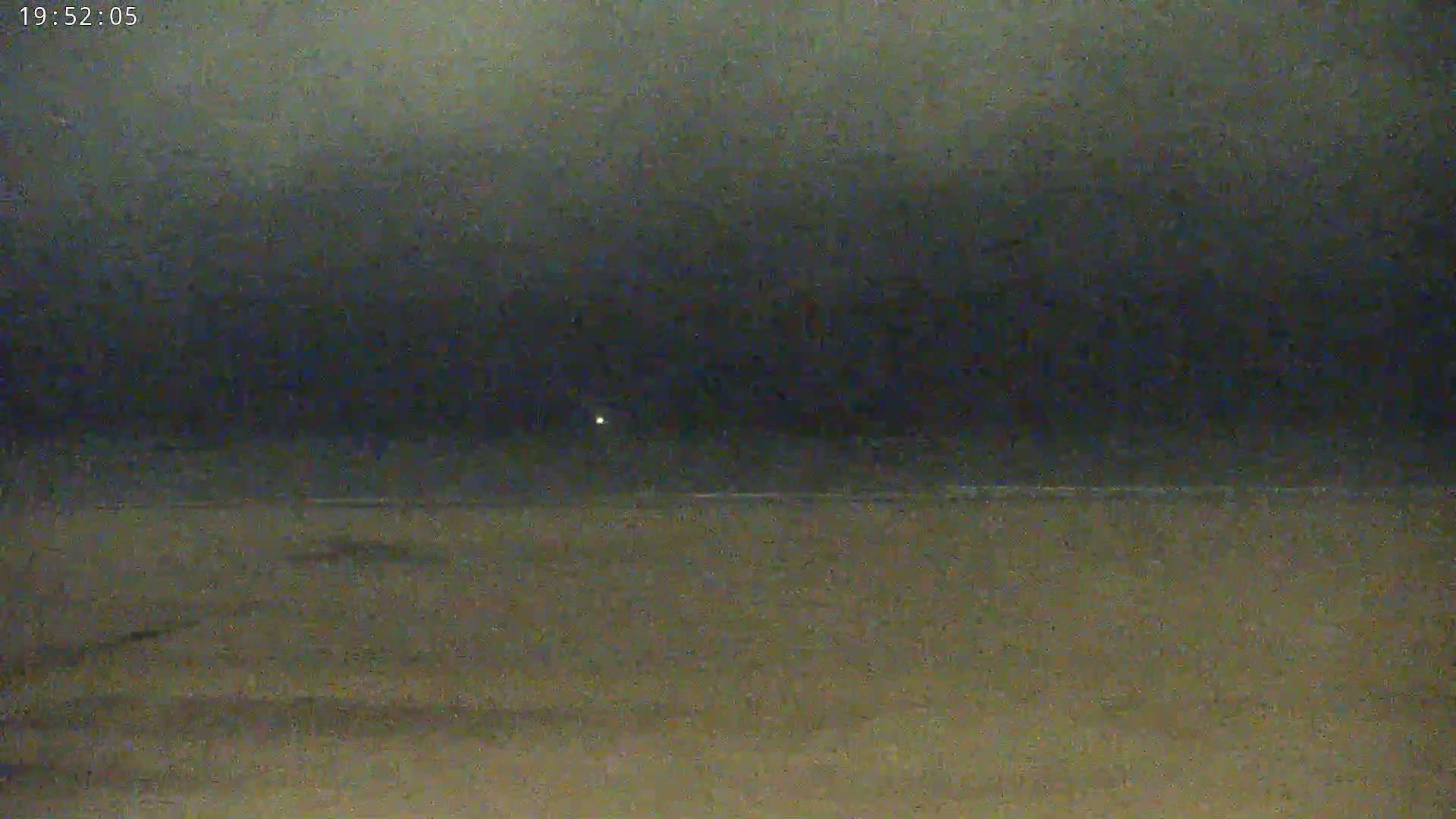 A dark, nighttime beach scene shows a mostly calm ocean under a cloudy sky.