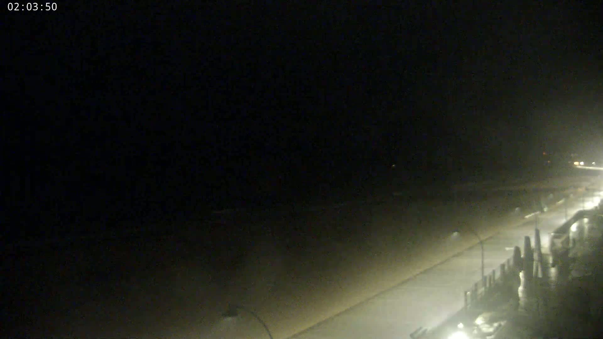 A nighttime view of a beach and boardwalk, with faintly visible lights and a dark, possibly overcast sky.