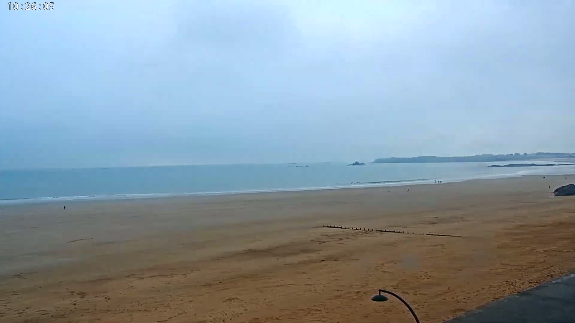 A wide sandy beach stretches to a calm, light-blue ocean under an overcast sky.