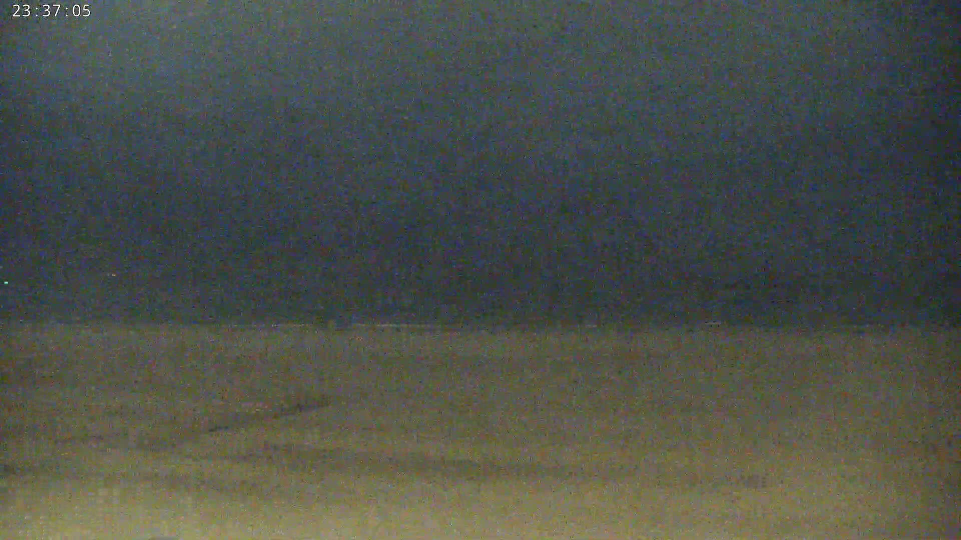 A dark, nighttime scene shows a flat, light-brown expanse of land under a dark, overcast sky.