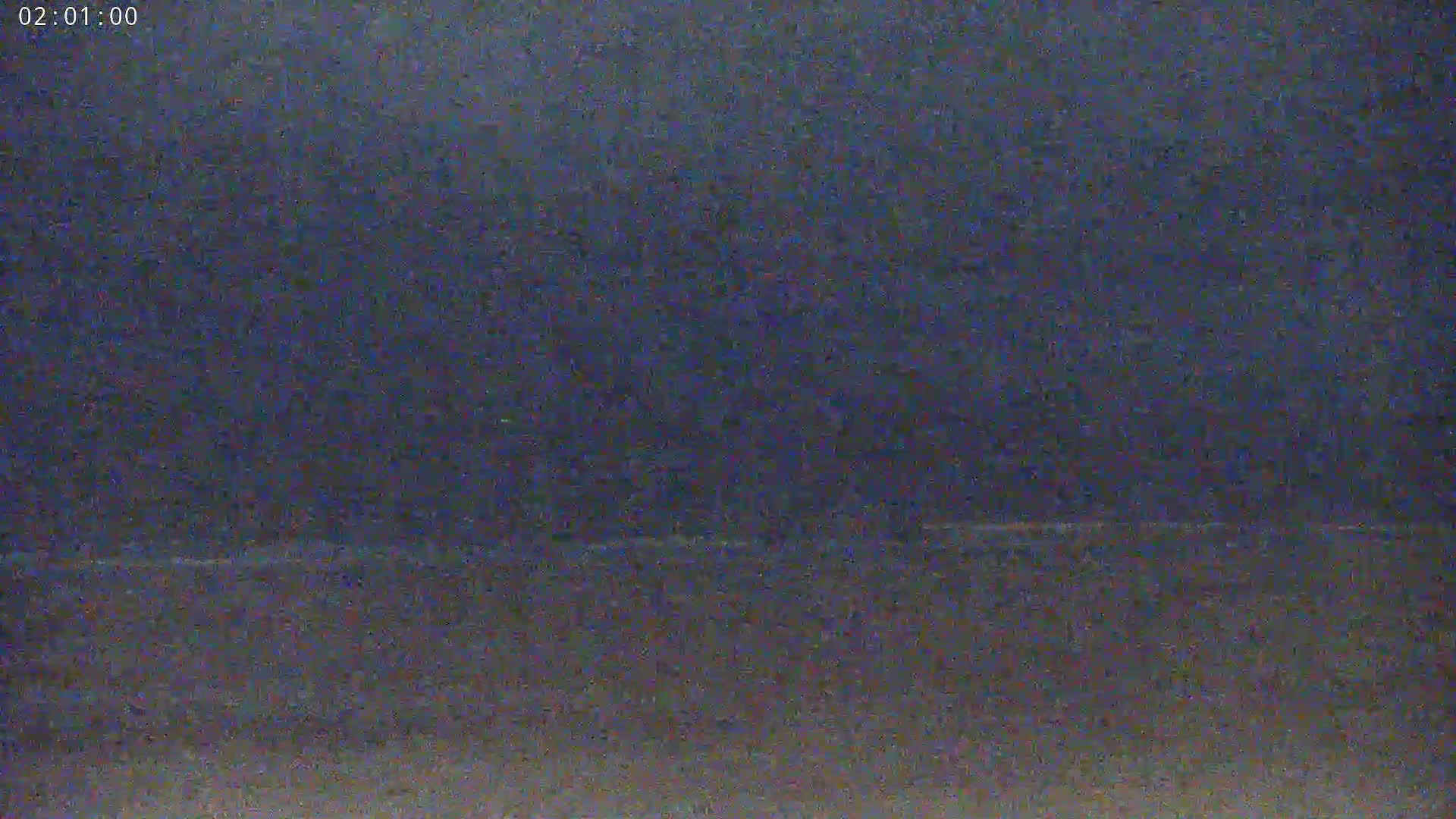 A dark, nighttime scene shows a blurry horizon line, possibly of water under a cloudy sky.