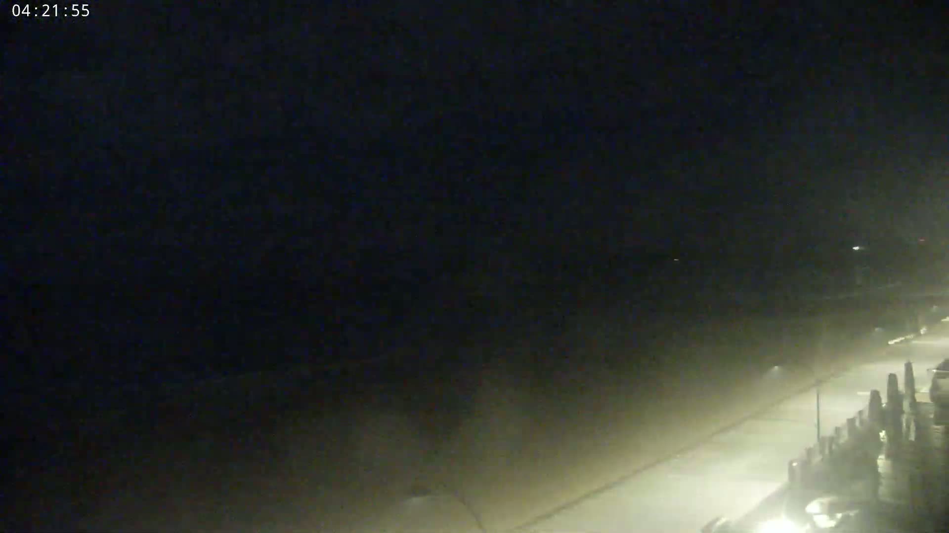 A nighttime, hazy scene shows a dimly lit street next to a body of water.