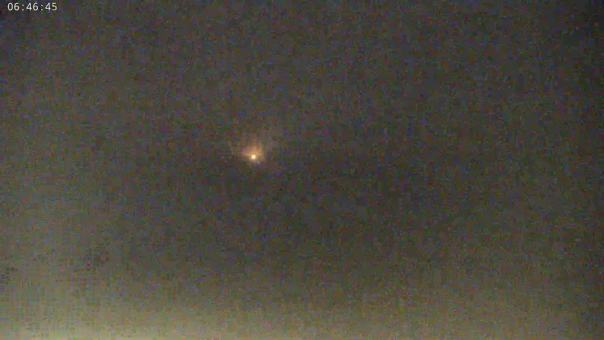 A small, bright light is visible in a dark, night sky.