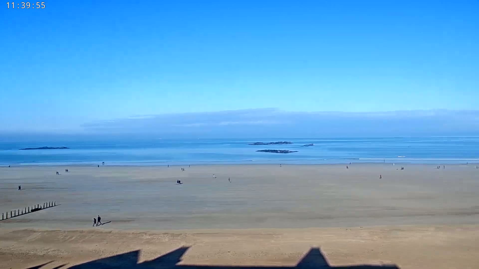 A wide, sandy beach stretches to a calm, blue ocean under a clear, blue sky.