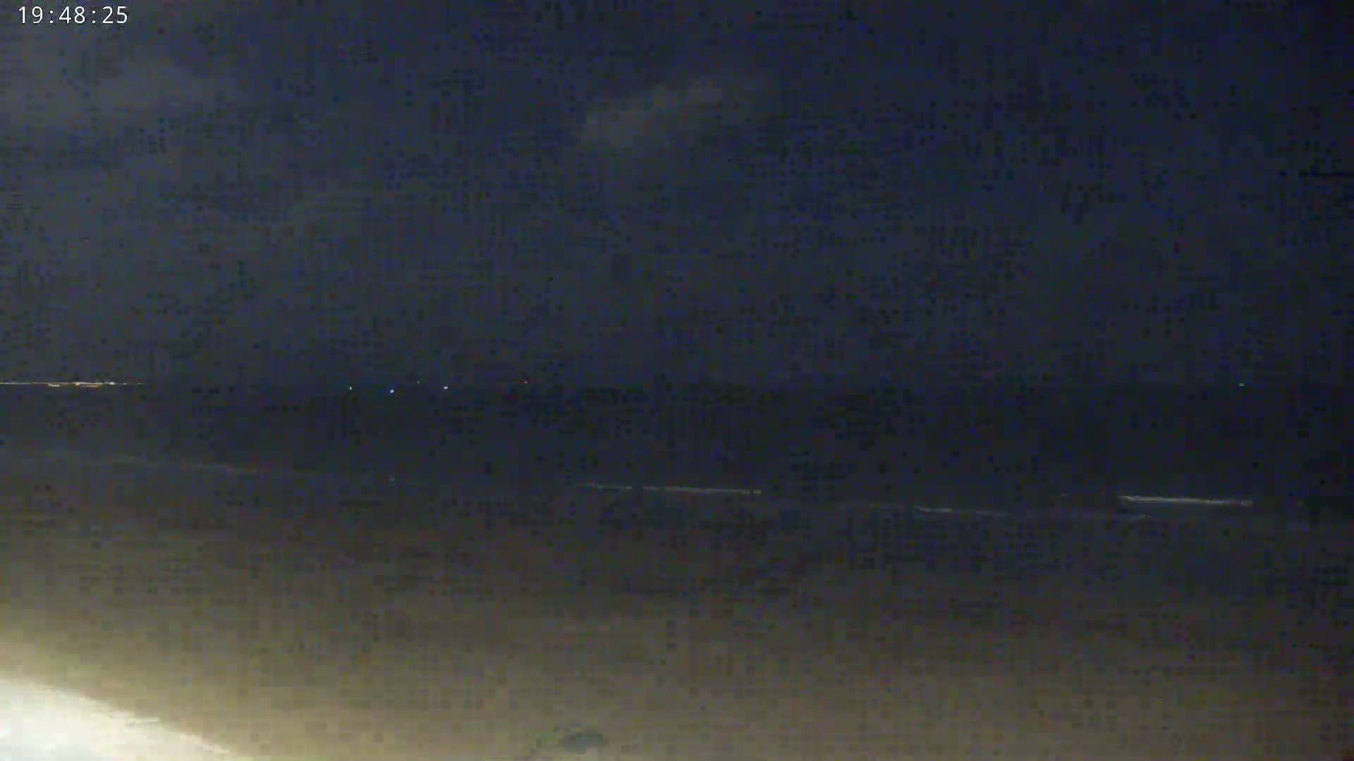 A dark beach at night shows a calm ocean under a mostly clear, dark sky.