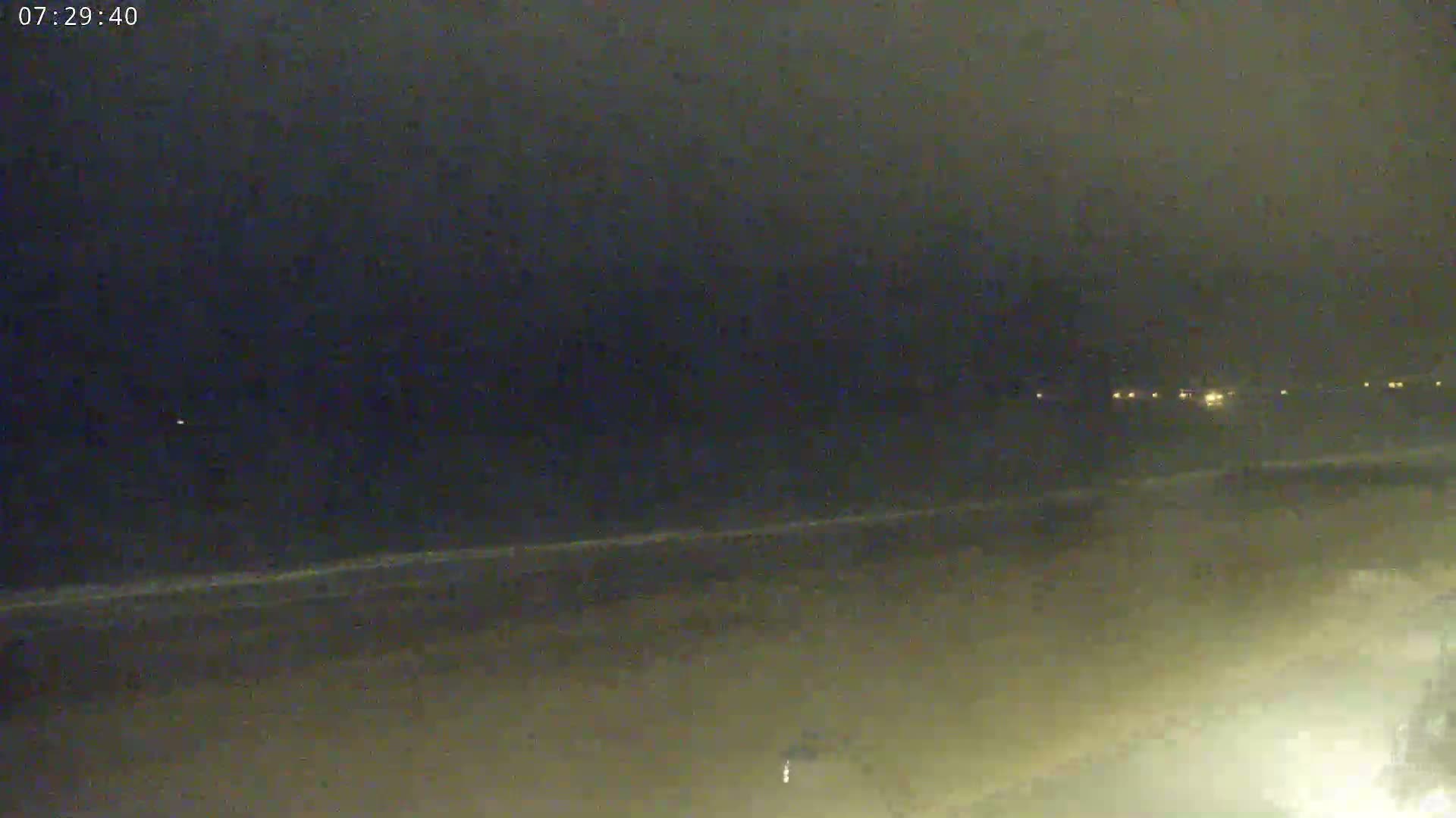 A dark, nighttime beach scene shows a dimly lit shoreline with faint waves and distant lights.