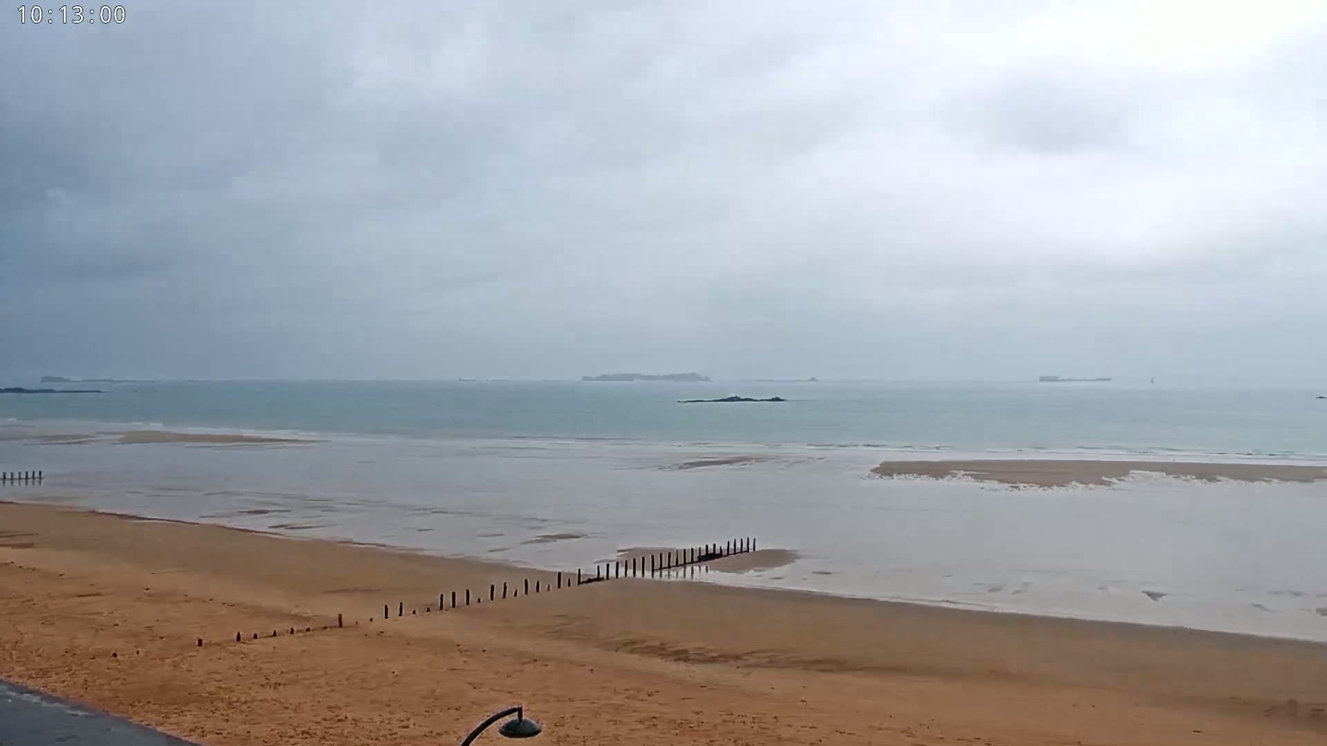 A sandy beach stretches out to a calm, light-blue sea under a cloudy, overcast sky.