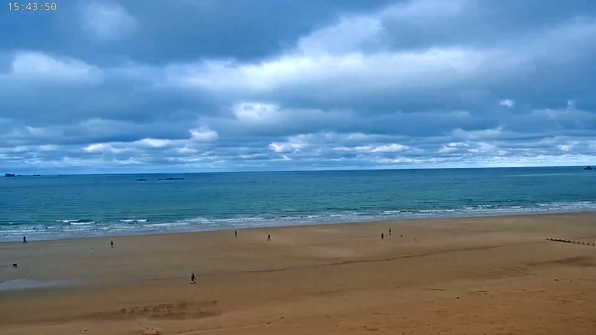 A wide sandy beach stretches towards a calm ocean under a mostly cloudy sky.