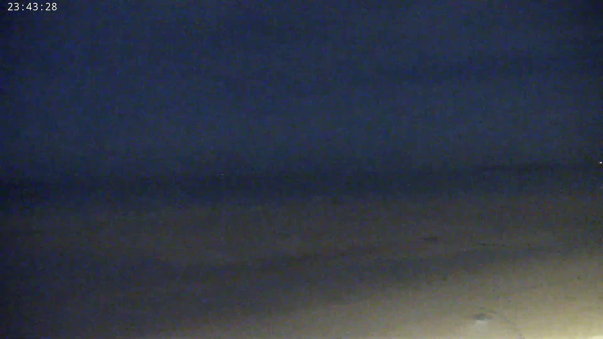 A dark, nighttime view shows a mostly flat, sandy area extending to a dark horizon under a clear, dark blue sky.