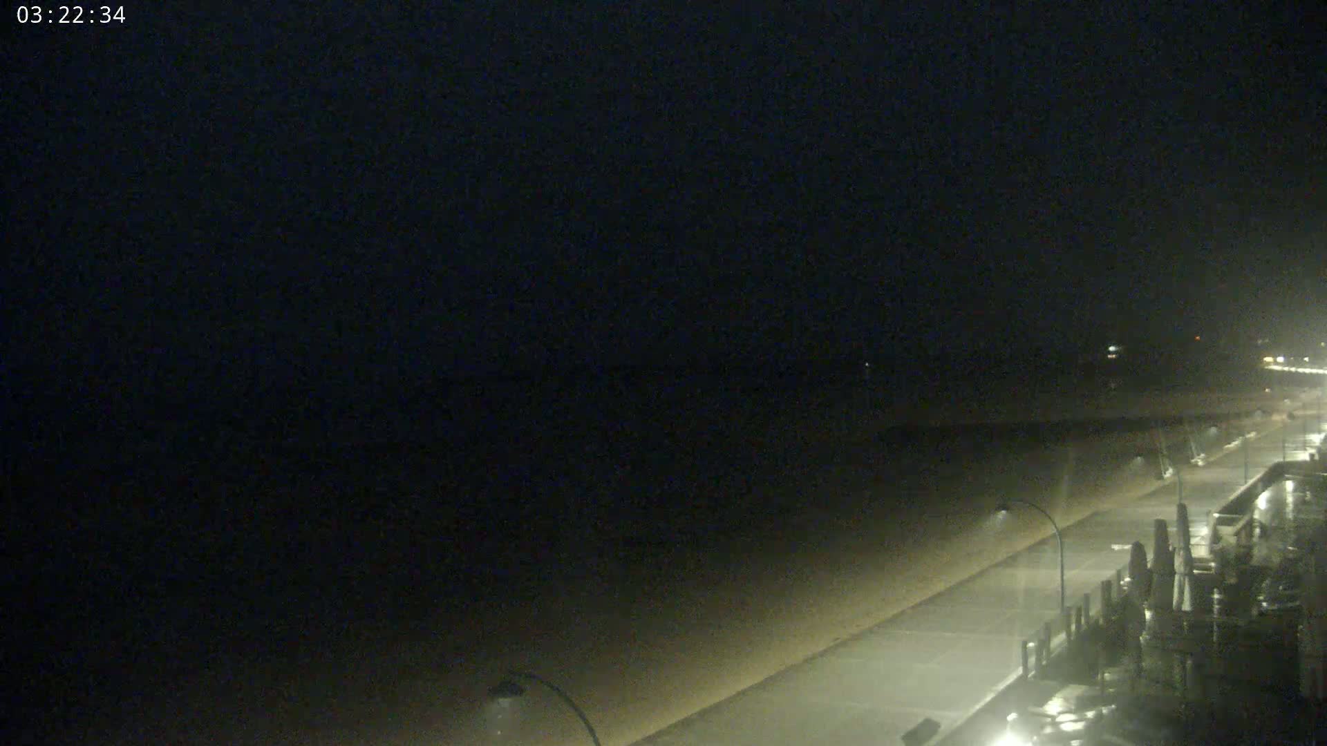 A nighttime view of a rain-swept beach with a boardwalk and streetlights.