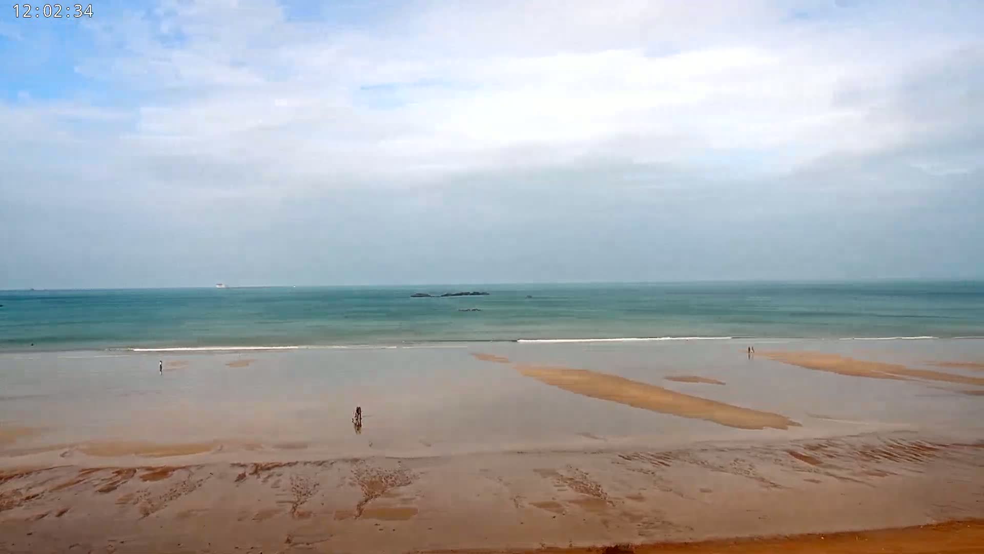 A wide sandy beach stretches to a calm teal ocean under a mostly cloudy sky.