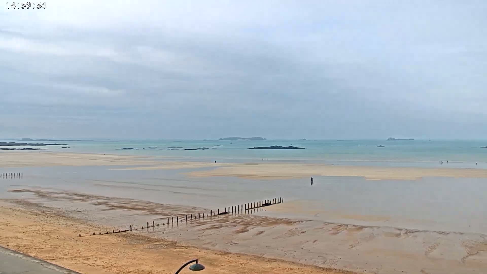 A wide sandy beach stretches to a calm, light-blue ocean under a cloudy sky.