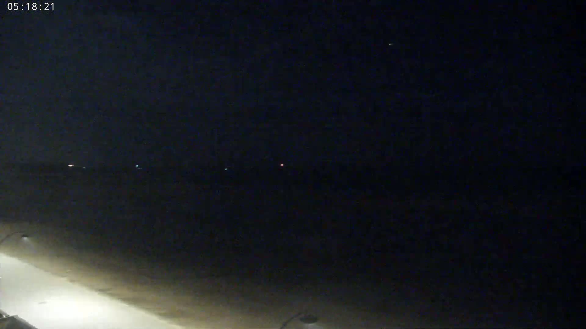 A nighttime view of a dark beach with faint lights on the horizon under a clear, dark sky.