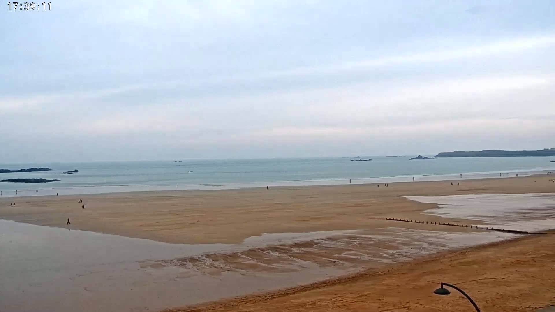 A wide sandy beach stretches to a calm ocean under an overcast sky.