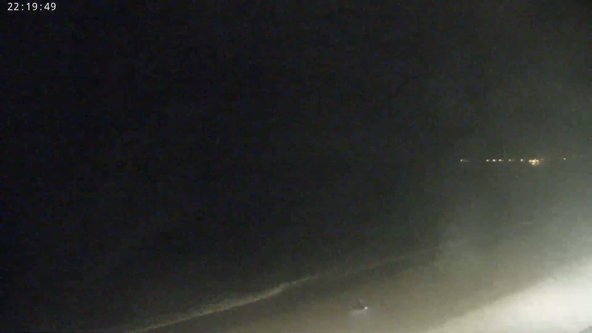 A dark nighttime beach scene shows a hazy, dimly lit ocean with faint waves and distant lights on the shore.