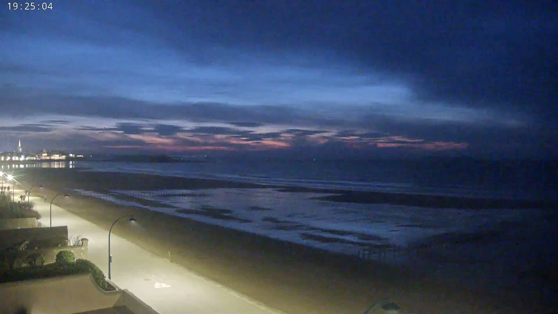 A long, sandy beach stretches out to a calm ocean under a twilight sky with streaks of pink and purple clouds.