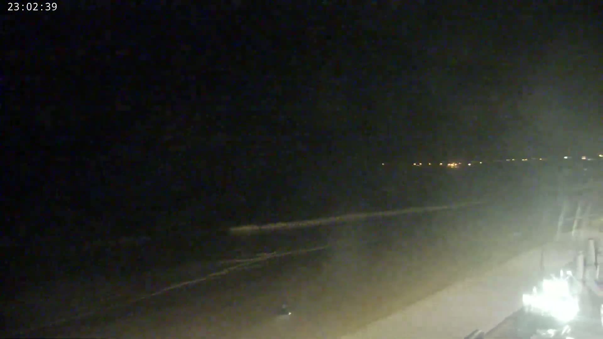 A dark, nighttime beach scene shows gently lapping waves and distant lights on the horizon.