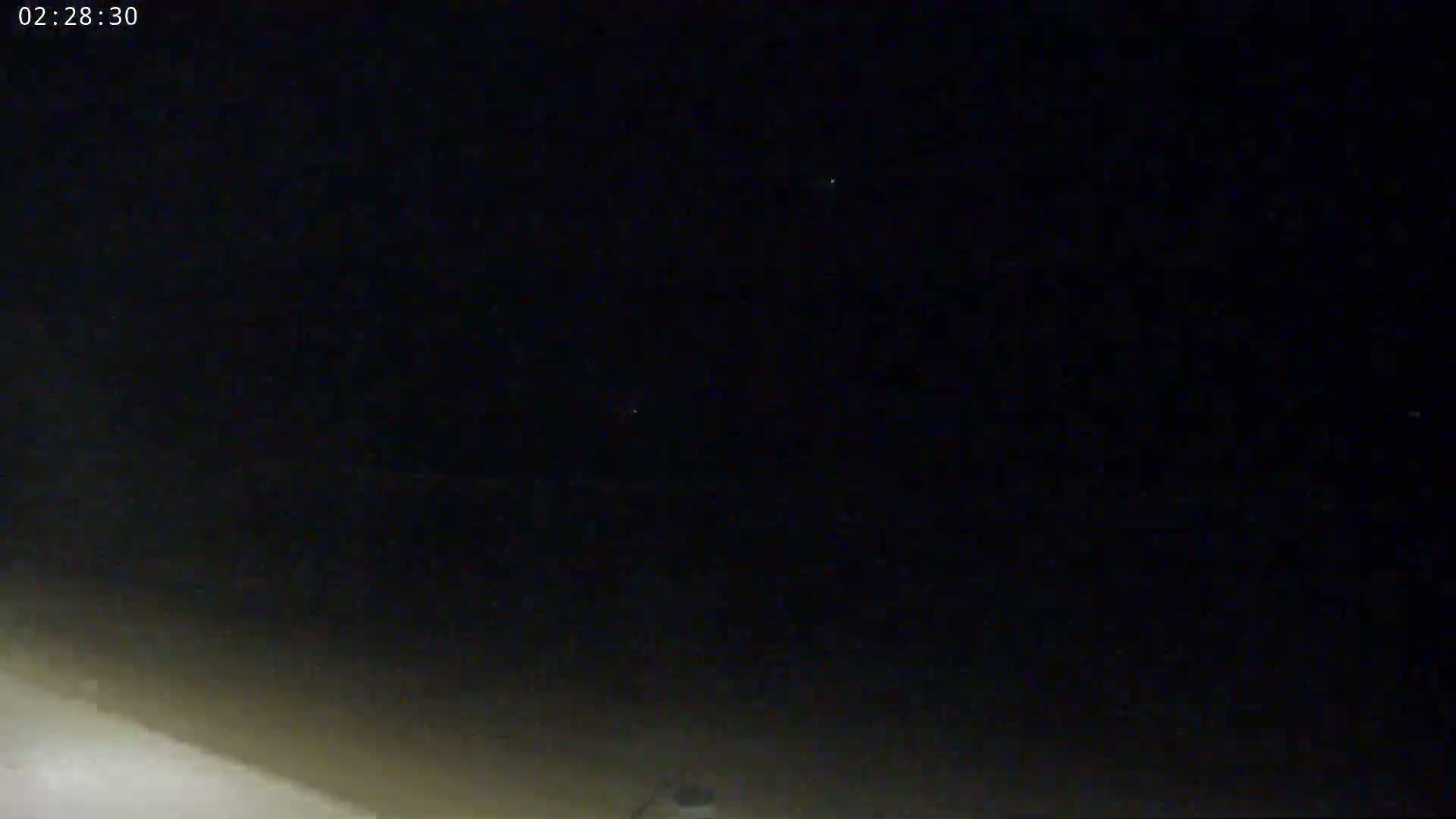A nighttime, low-light outdoor scene shows a dark sky with a few faint lights, possibly stars, and a brighter area at the bottom, possibly ground illuminated by a light source.