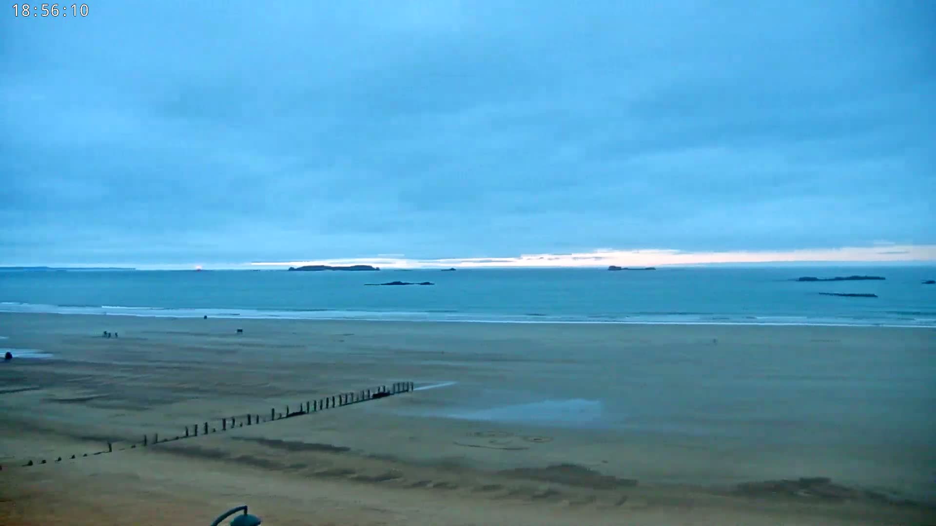A wide, sandy beach stretches to a calm, teal ocean under a mostly clear, light-blue sky.