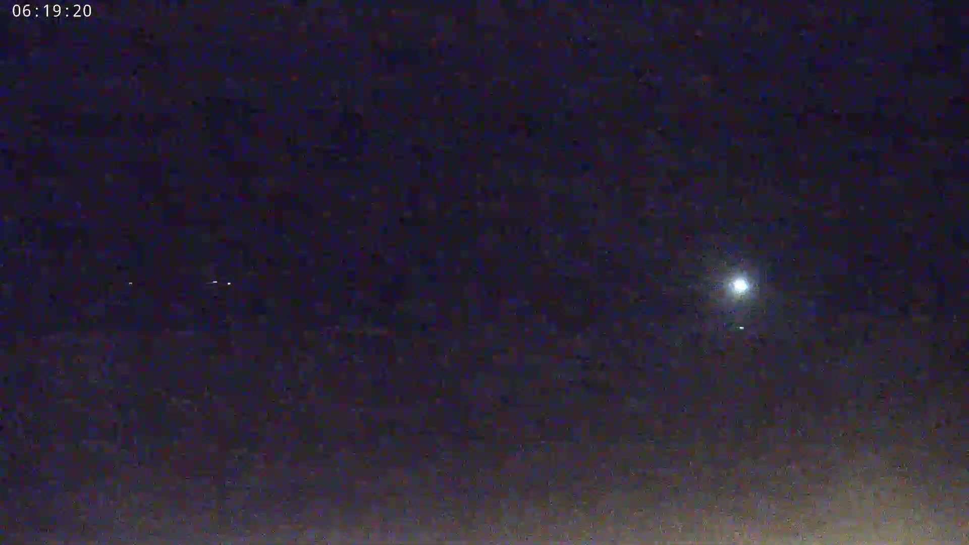 A nighttime, outdoor scene shows a bright light, possibly the moon, and several fainter lights in the dark sky.