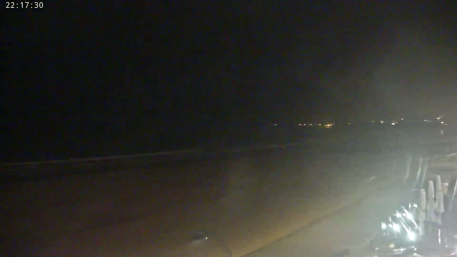 A dark, nighttime beach scene shows a dimly lit shoreline and ocean under a clouded sky.