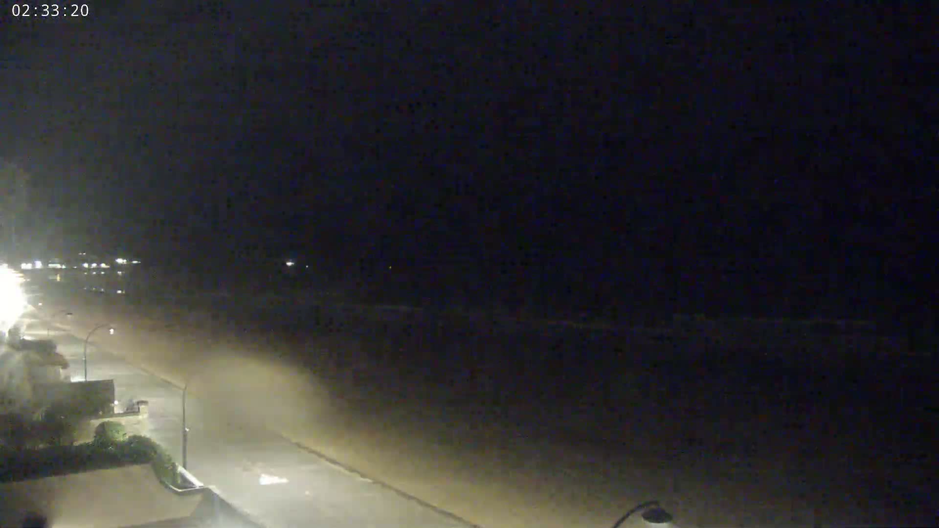 A nighttime view shows a dimly lit beach and road with some buildings and vegetation visible on the left.