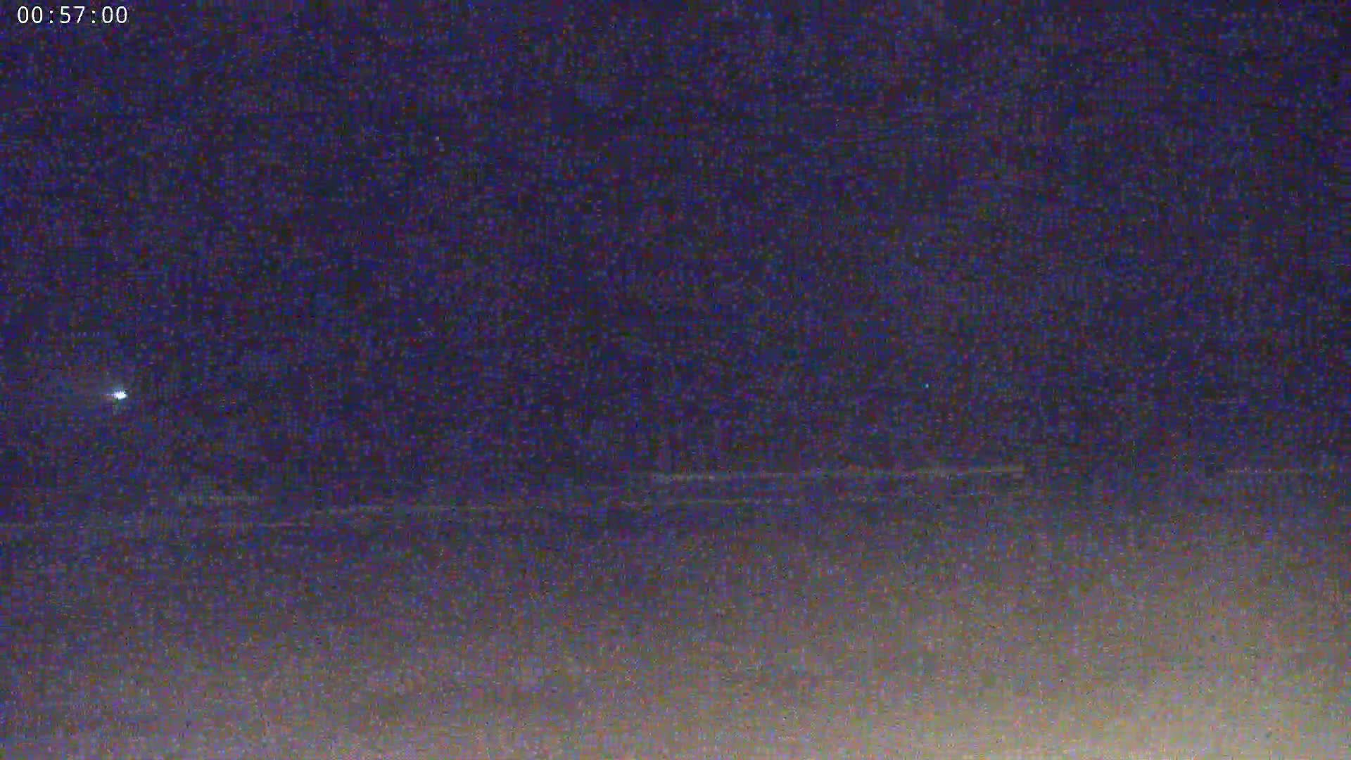A dark, nighttime scene shows a faint horizon line and a single, bright light in the distance under a clear, starless sky.
